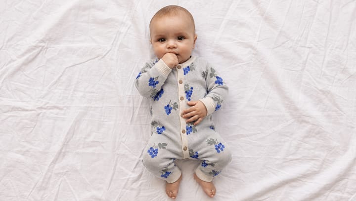 Baby in een boxpakje met blauwe bloemen, liggend op een wit laken
