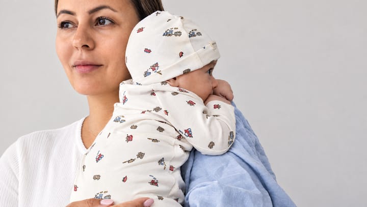 Mama met haar baby in een mutsje en pakje met treintjesprint op de schouder